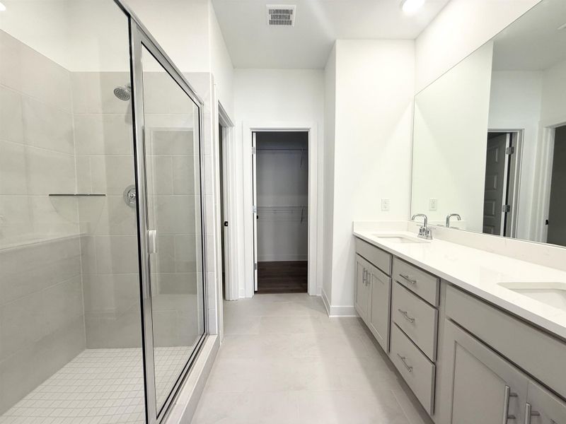 Bathroom featuring double vanity, a stall shower, a walk in closet, and light tile patterned floors