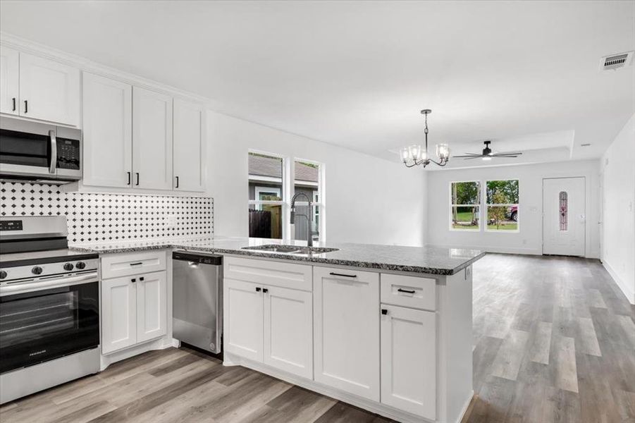 Kitchen with stainless steel appliances, dark stone countertops, ceiling fan with notable chandelier, light hardwood / wood-style flooring, and white cabinets