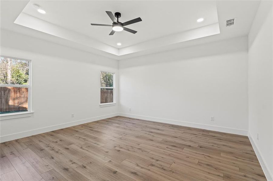 Empty room with a raised ceiling, wood finished floors, recessed lighting, and a ceiling fan