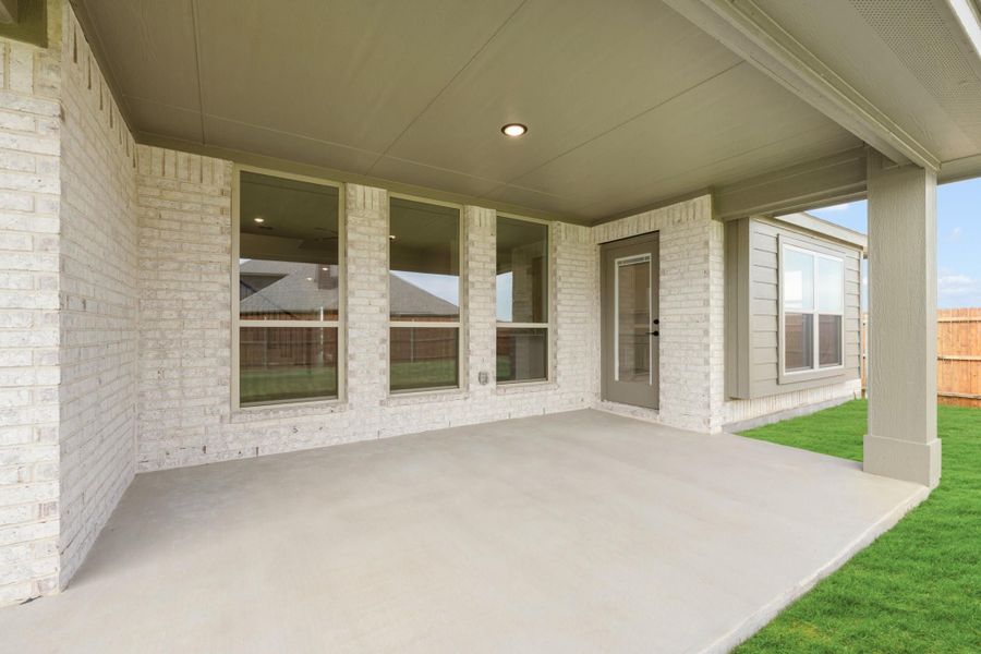 Covered back patio with concrete floor, white brick exterior, and back door entry overlooking green lawn