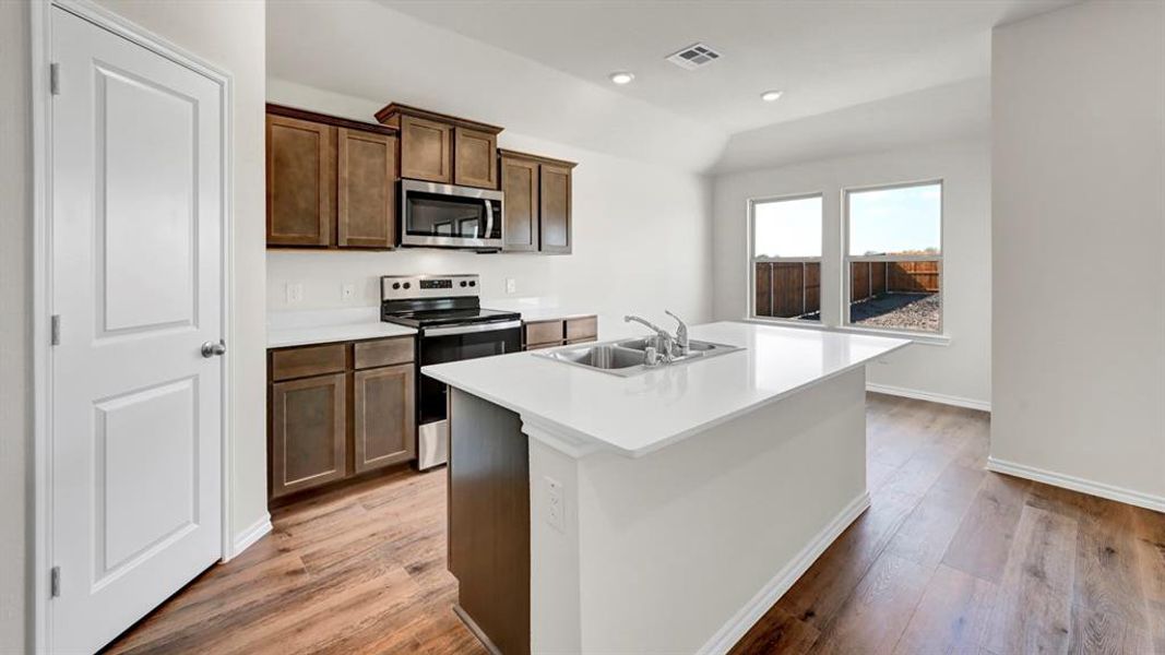 Modern kitchen featuring wood-finish flooring, white countertops, dark wood cabinetry, a built-in microwave, and a double basin sink within the island