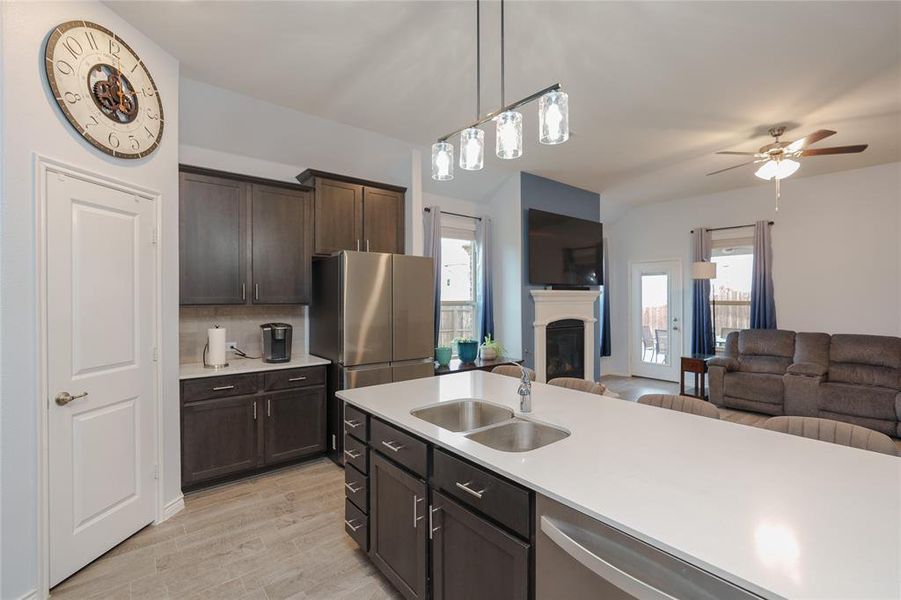 Kitchen with appliances with stainless steel finishes, dark brown cabinetry, sink, light hardwood / wood-style floors, and hanging light fixtures