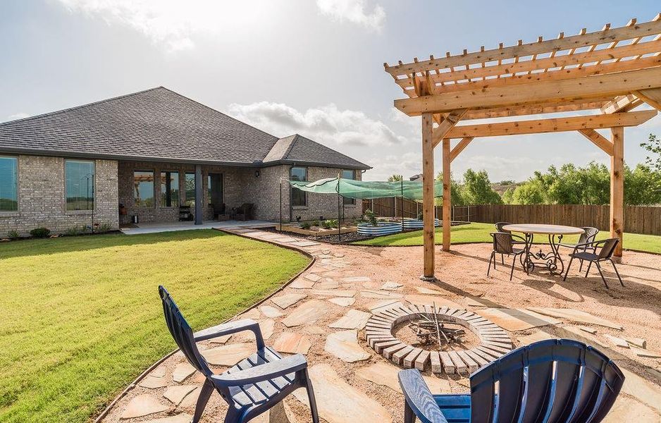 Expansive backyard featuring a covered patio extended to a wooden pergola living space, vegetable garden, a large grassy area, and a privacy fence.