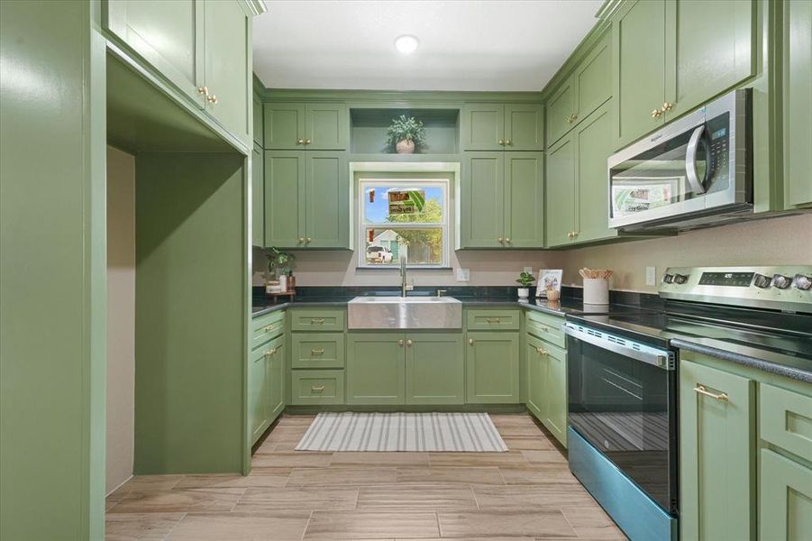 Kitchen featuring green cabinetry, appliances with stainless steel finishes, open shelves, wood tiled floors, and dark stone countertops Kitchen featuring green cabinetry, appliances with stainless steel finishes, open shelves, wood tiled floors, and dark stone countertops