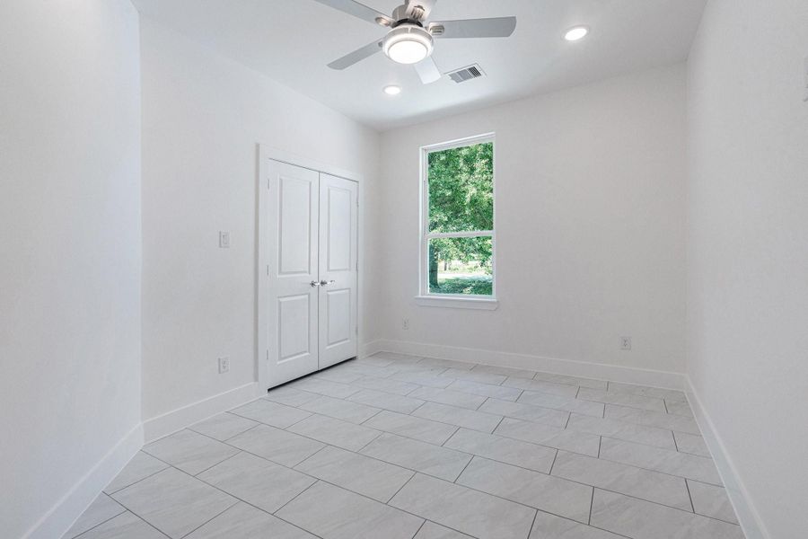 This room features bright white walls and tiled flooring, creating a fresh and modern feel. It includes a large window for natural light, a ceiling fan, and a closet with double doors, perfect for additional storage. This room features bright white walls and tiled flooring, creating a fresh and modern feel. It includes a large window for natural light, a ceiling fan, and a closet with double doors, perfect for additional storage.