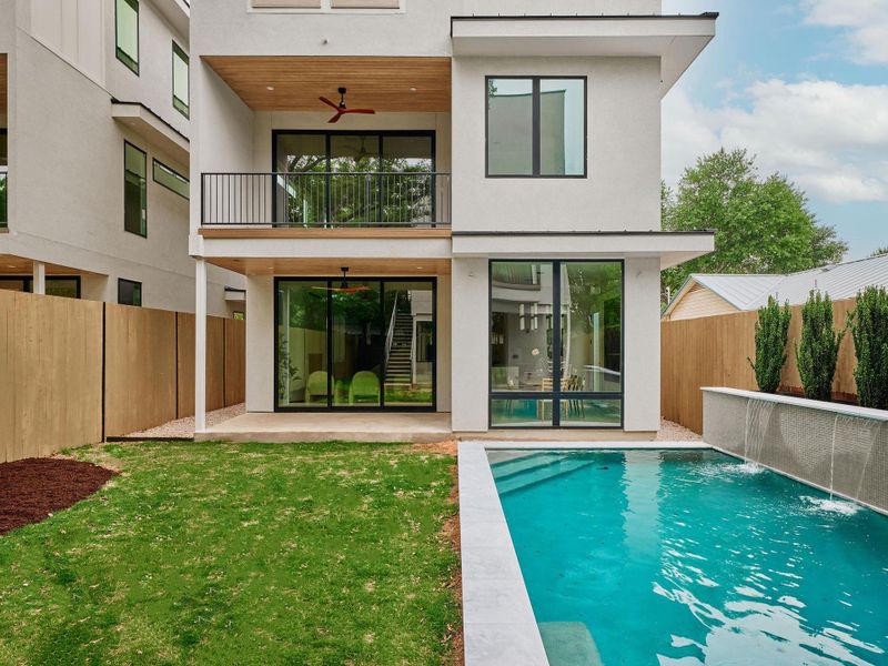 Modern exterior featuring a private swimming pool with a waterfall feature, a covered ground-floor patio, an upper-level balcony with a wood-finish ceiling, and expansive glass doors