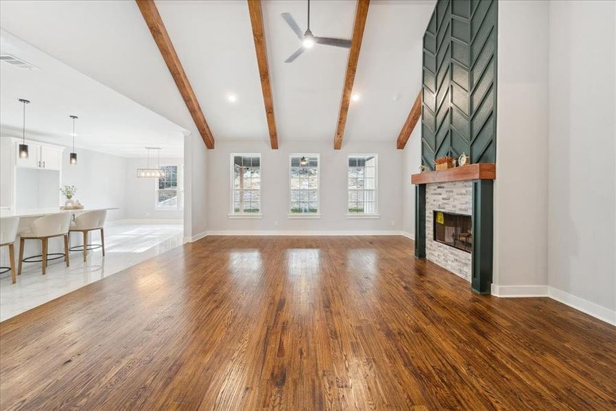 Unfurnished living room with a brick fireplace, dark hardwood / wood-style floors, vaulted ceiling with beams, and ceiling fan