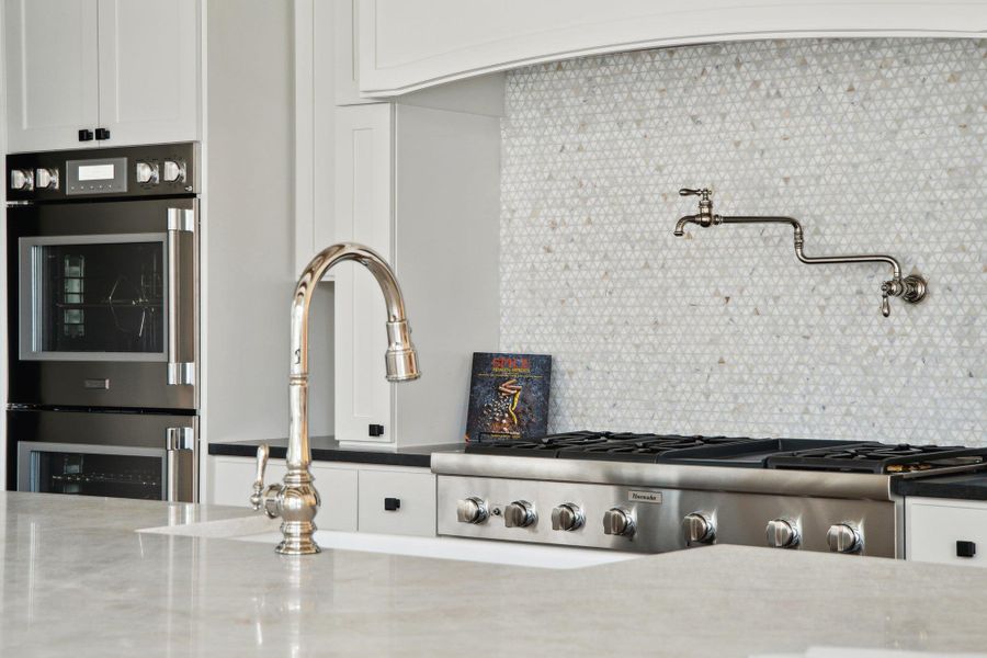 Interior details featuring stainless steel double oven, backsplash, and white cabinetry