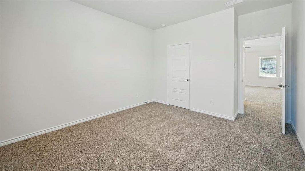 Carpeted interior room featuring white painted walls and trim, a five-panel interior door with a dark handle, and an open doorway revealing an additional carpeted room beyond