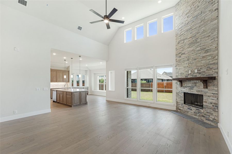 Open living room with vaulted ceiling, stone fireplace, hardwood floors, and open kitchen beyond Open living room with vaulted ceiling, stone fireplace, hardwood floors, and open kitchen beyond