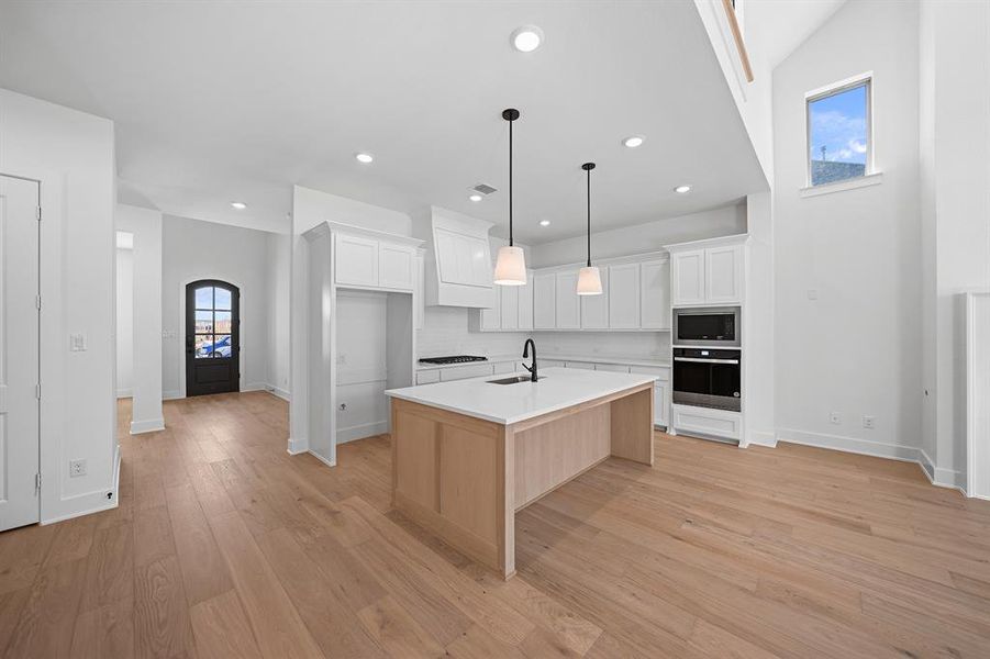 Kitchen featuring white cabinetry, stainless steel appliances, an island with sink, arched walkways, and light wood finished floors