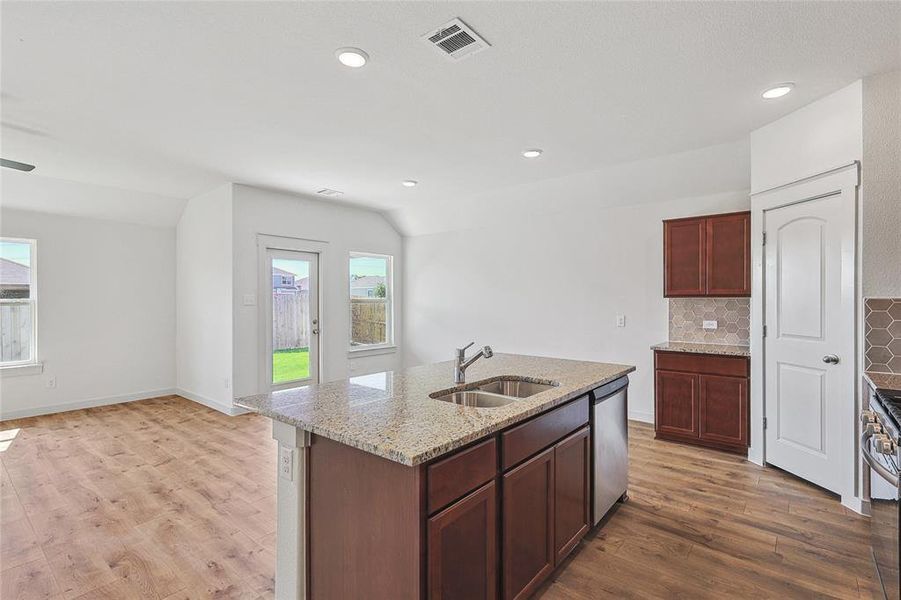 Kitchen with lofted ceiling, hardwood / wood-style floors, stainless steel appliances, sink, and a center island with sink