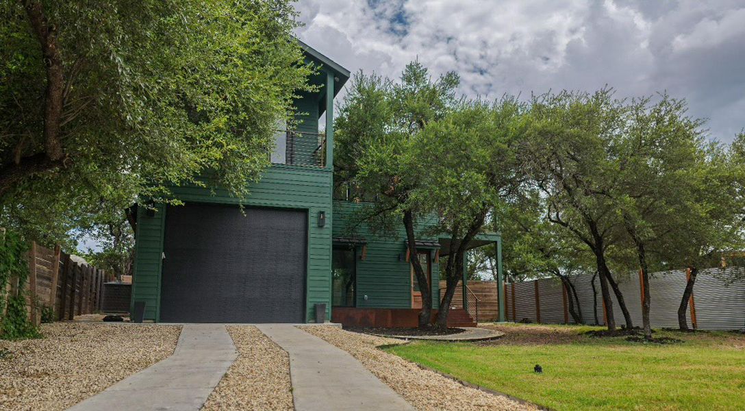 A striking nature green home with a dark garage door, nestled amongst mature trees and a long private driveway. A striking nature green home with a dark garage door, nestled amongst mature trees and a long private driveway.