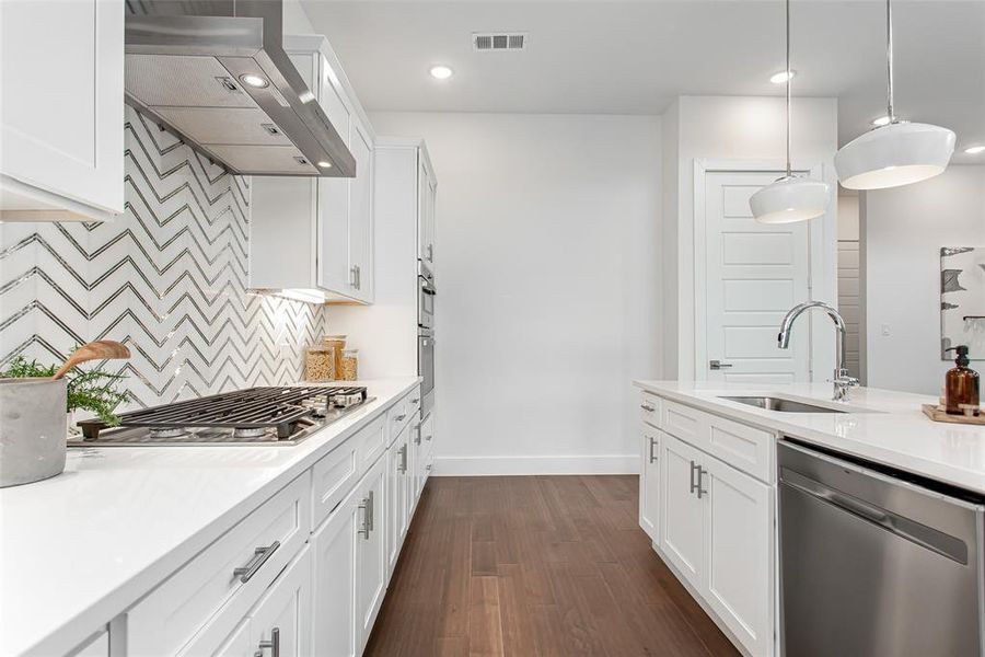 Kitchen featuring wall chimney range hood, dark hardwood / wood-style flooring, stainless steel appliances, decorative light fixtures, and sink