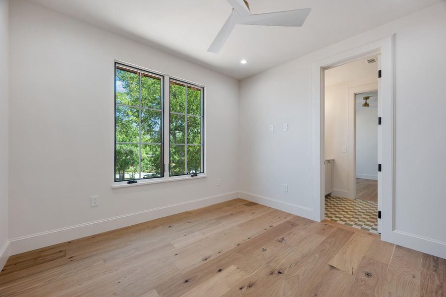 Warm hardwood floors complement clean white walls and a large window framing leafy green views.