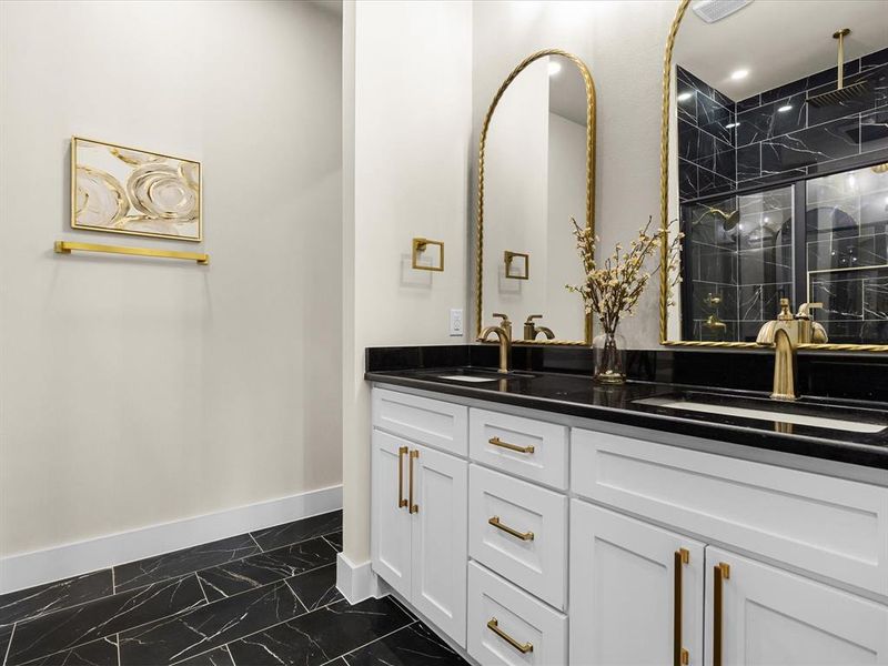 Dual vanity with white cabinetry and gold-tone hardware, black countertops, and two arched gold-framed mirrors