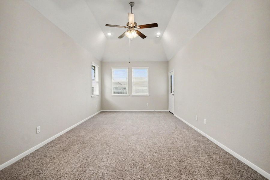 Spacious bedroom with vaulted ceilings, neutral tones, and plenty of natural light, complemented by plush carpeting and a stylish ceiling fan.