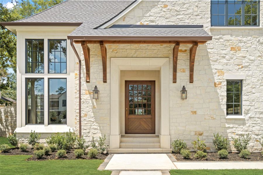 The home’s striking entry pairs a handcrafted limestone façade with an oversized custom mahogany pivot door. Soaring steel-framed windows and warm architectural wood detailing create a distinctive first impression, setting the tone for the craftsmanship found throughout the home. The home’s striking entry pairs a handcrafted limestone façade with an oversized custom mahogany pivot door. Soaring steel-framed windows and warm architectural wood detailing create a distinctive first impression, setting the tone for the craftsmanship found throughout the home.