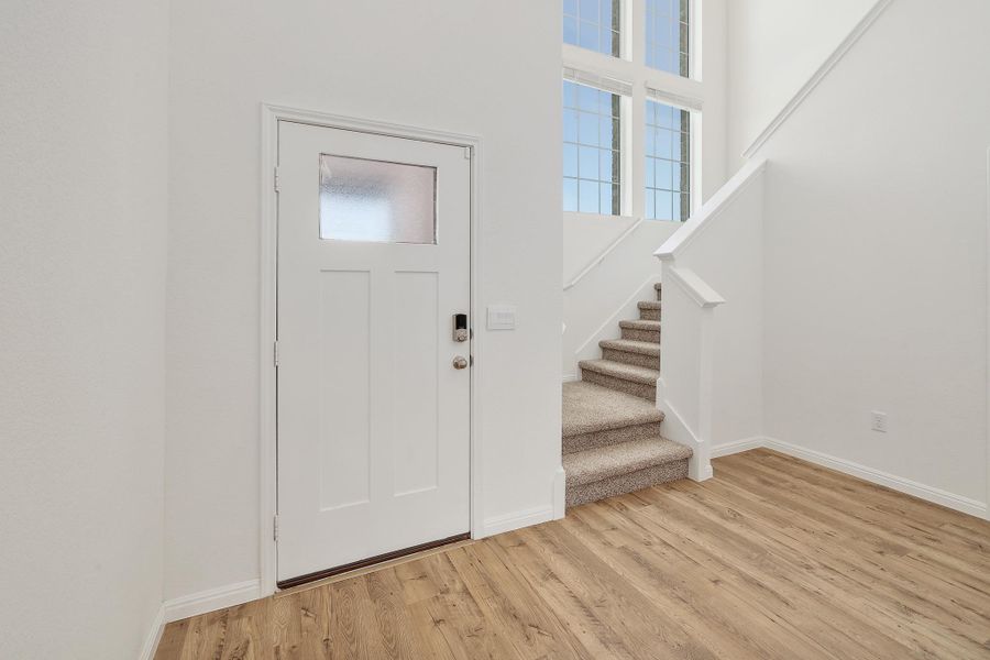 Foyer featuring wood-finish flooring, a white paneled entry door with frosted glass, and a carpeted staircase with white railings Foyer featuring wood-finish flooring, a white paneled entry door with frosted glass, and a carpeted staircase with white railings