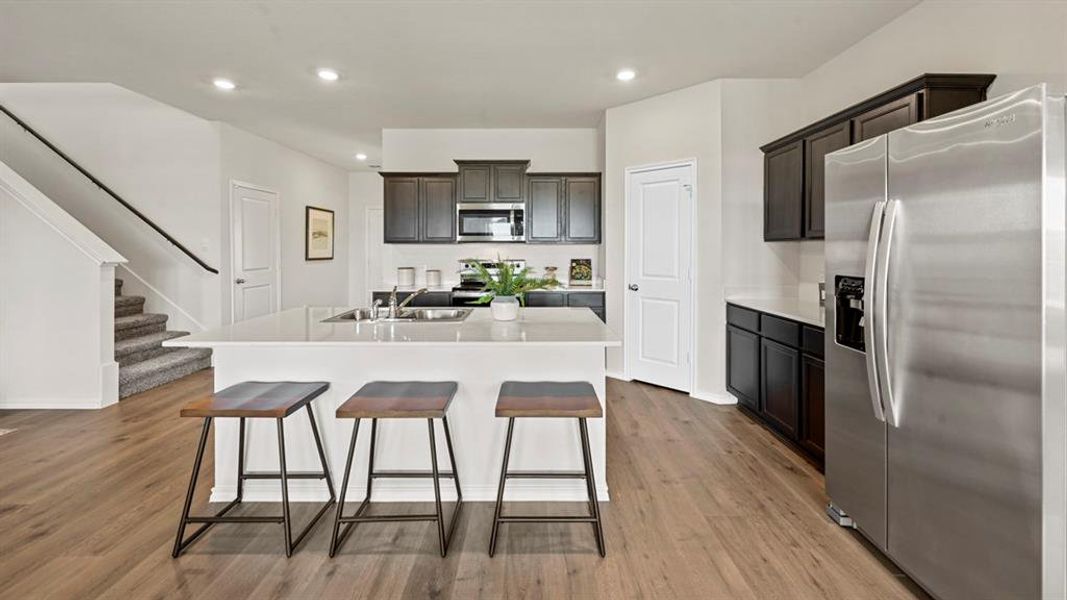 The kitchen features dark wood cabinetry, a stainless steel refrigerator, and a large island with three stools The kitchen features dark wood cabinetry, a stainless steel refrigerator, and a large island with three stools