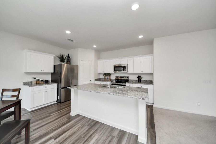 Modern kitchen with sleek stainless steel appliances, granite countertops, and ample white cabinetry, featuring a spacious island and stylish wood flooring.