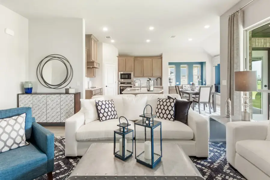Open-concept living room with white sofa, blue accents, and kitchen visible in background