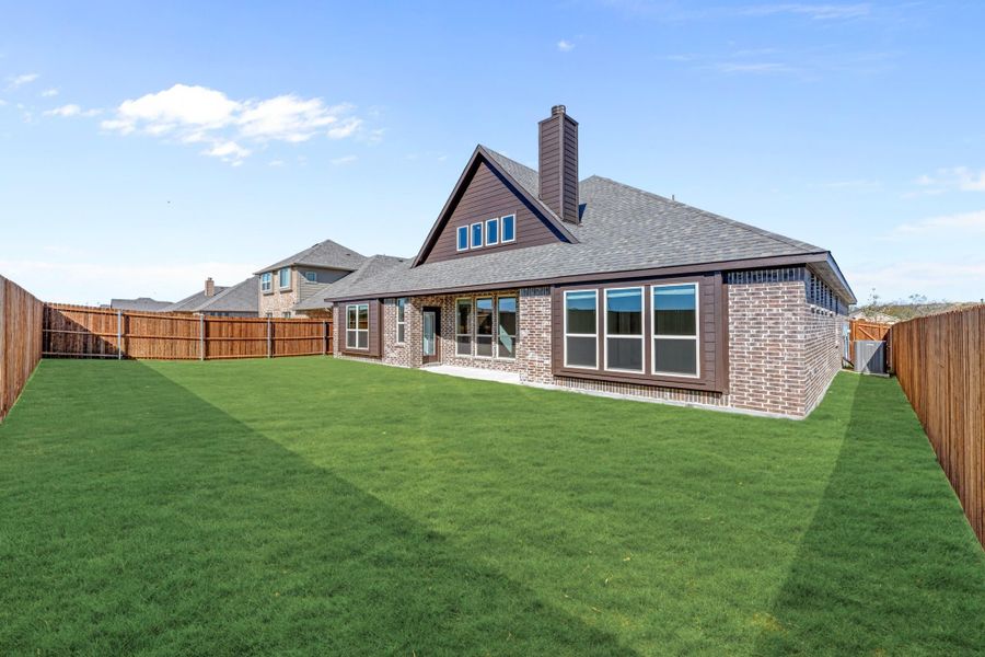 Rear view of brick home with large fenced backyard, green lawn, and chimney Rear view of brick home with large fenced backyard, green lawn, and chimney