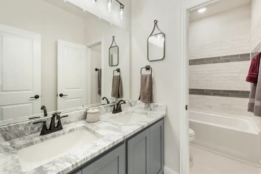 Bathroom with double vanity, gray cabinets, marble countertops, and tiled bathtub surround