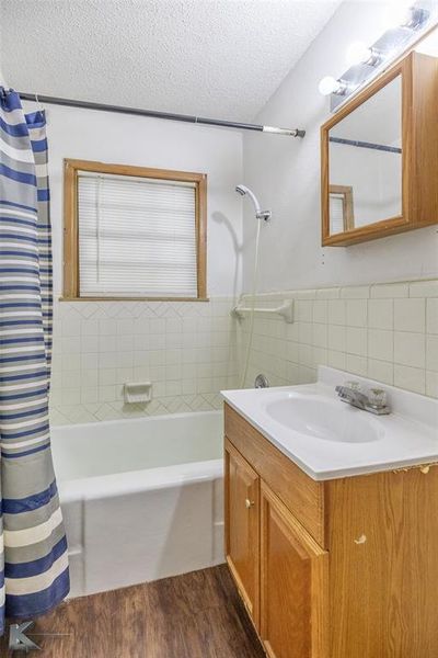 Bathroom featuring a textured ceiling, wood finished floors, vanity, shower / bath combination with curtain, and tile walls