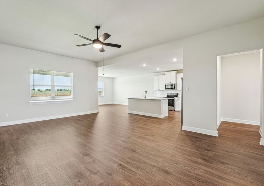 Open-concept family room featuring a ceiling fan, wood-look vinyl flooring, and a sightline into the kitchen and dining area. Open-concept family room featuring a ceiling fan, wood-look vinyl flooring, and a sightline into the kitchen and dining area.