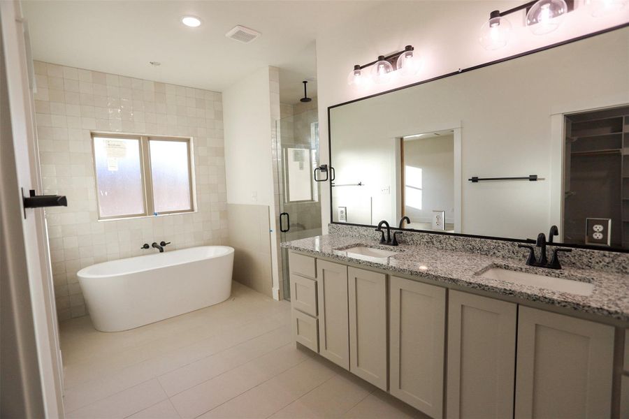 Bathroom with double vanity, tile walls, a shower stall, a freestanding bath, and light tile patterned flooring