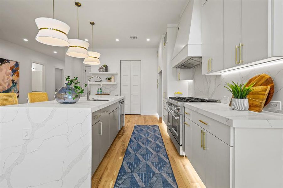 Kitchen with light hardwood / wood-style floors, stainless steel appliances, custom exhaust hood, and pendant lighting