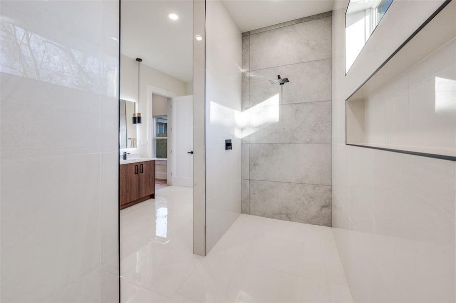 Open-concept shower featuring a rainfall showerhead, large format tile walls, and integrated shelving