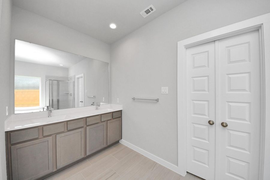 Enhance your daily routine at the refined vanity area, which boasts dual sinks, sleek countertops in soft, light tones, and modern fixtures. Sample photo of completed home with similar floor plan. Actual colors and selections may vary.