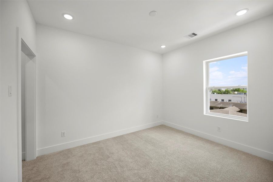 This secondary bedroom on the third level is bright, carpeted, white walls, recessed lighting, and a window offering natural light and an outdoor view.