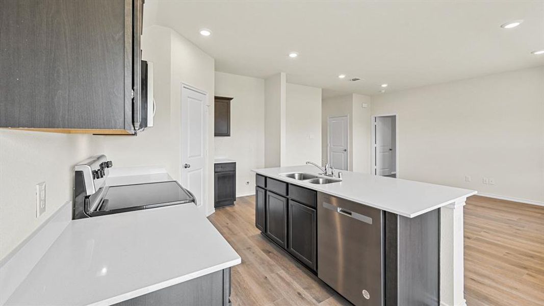 Kitchen with stainless steel appliances, a kitchen island with sink, recessed lighting, light wood-type flooring, and dark wood finish cabinetry