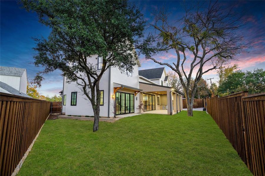 Expansive backyard featuring a manicured lawn, full privacy fencing, and two mature trees