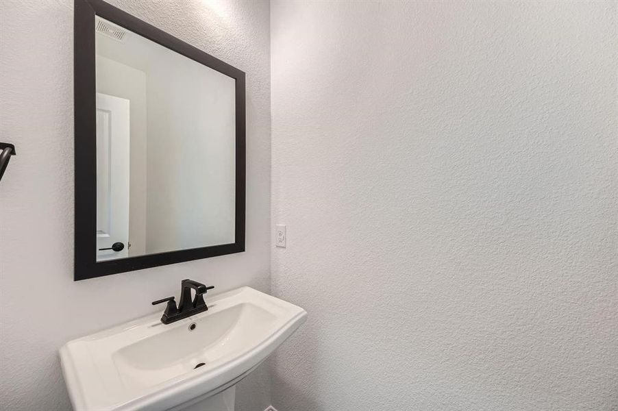 Pedestal sink with a matte black faucet and a framed wall mirror Pedestal sink with a matte black faucet and a framed wall mirror