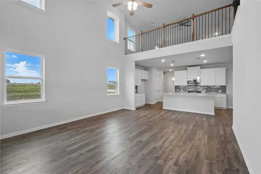 Unfurnished living room featuring a towering ceiling, dark wood-style flooring, and ceiling fan