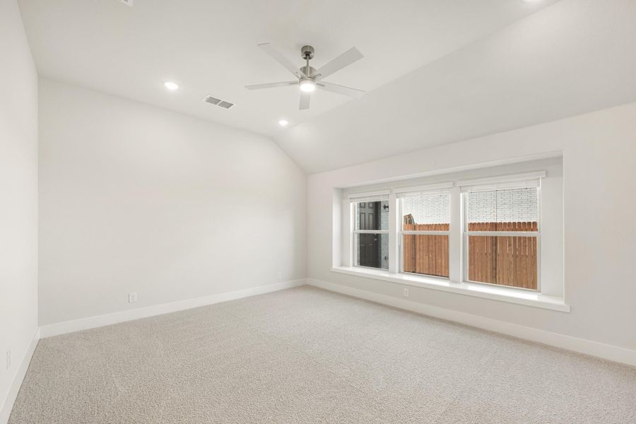 Empty bedroom with vaulted ceiling, ceiling fan, carpet flooring, and large triple window