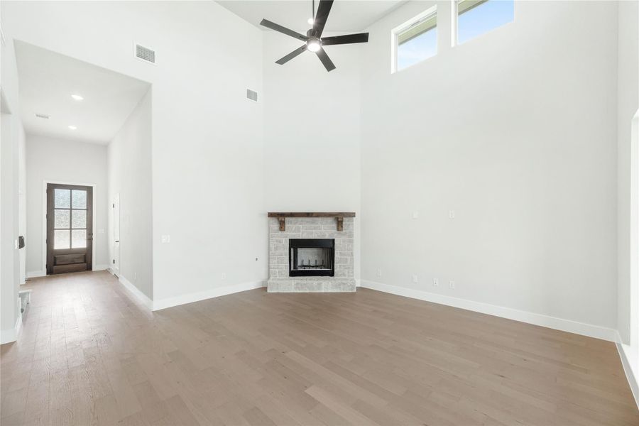 Open living room with high ceilings, stone fireplace, ceiling fan, and light hardwood floors Open living room with high ceilings, stone fireplace, ceiling fan, and light hardwood floors