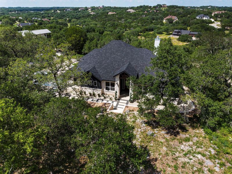 An aerial perspective reveals this residence nestled among a lush, tree-filled landscape.