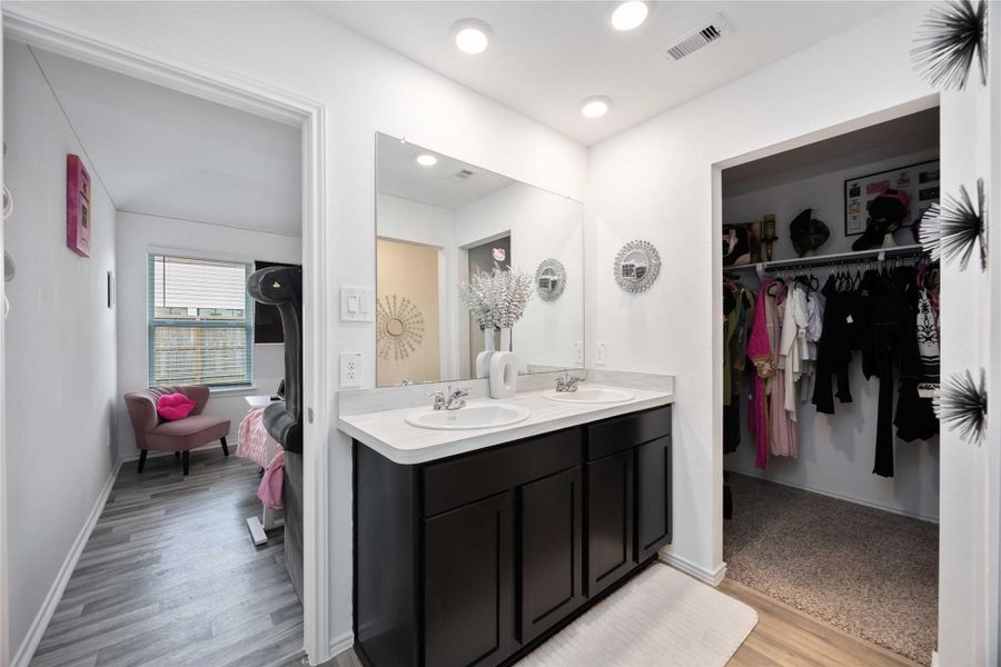 This photo showcases a modern bathroom with a dual-sink vanity and dark cabinets. It connects to a walk-in closet