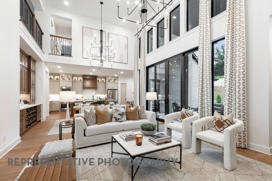 Living room featuring a chandelier, a high ceiling, light wood-style floors, baseboards, and recessed lighting Living room featuring a chandelier, a high ceiling, light wood-style floors, baseboards, and recessed lighting