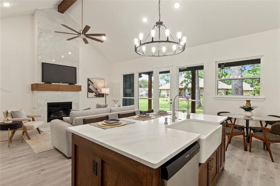 Kitchen with dishwasher, high vaulted ceiling, light wood-type flooring, a sink, and a high end fireplace