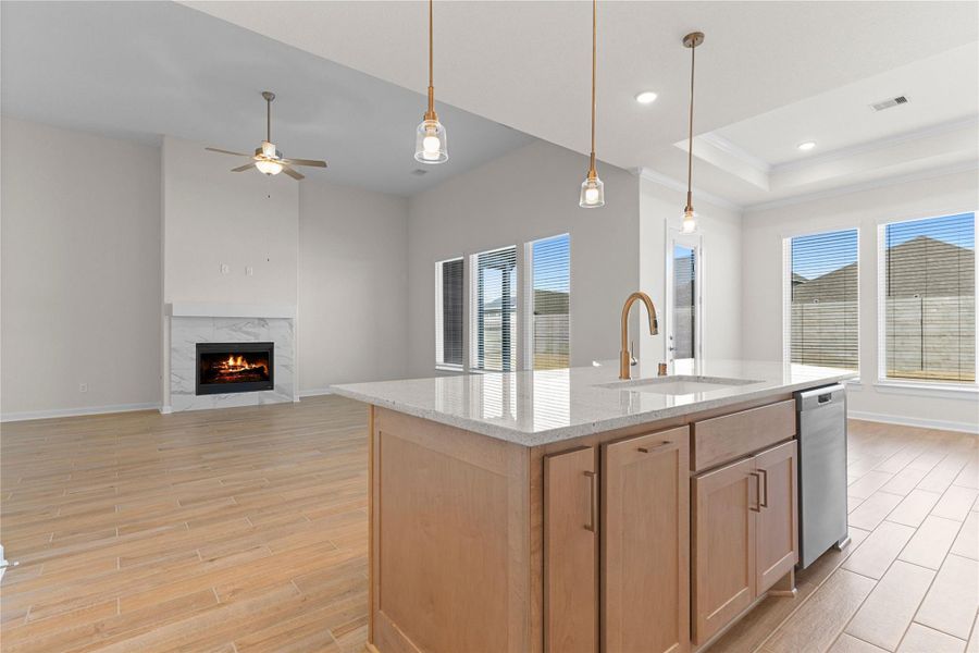 From this angle, the oversized kitchen island opens seamlessly to the family room, creating a warm and connected living space where wood like tile flooring, pendant lighting, and a cozy fireplace come together beautifully.