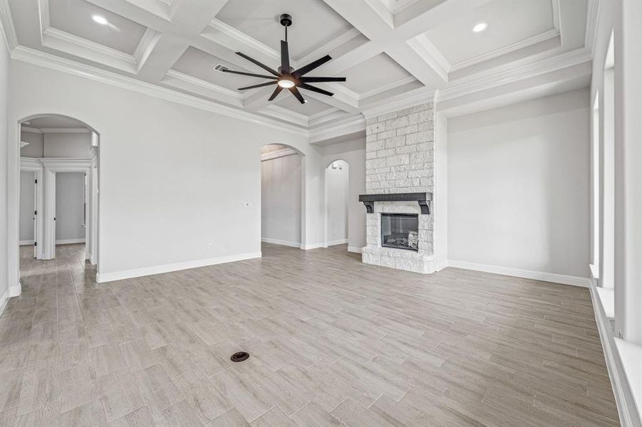 Unfurnished living room with arched walkways, a ceiling fan, light wood-style floors, beam ceiling, and a stone fireplace
