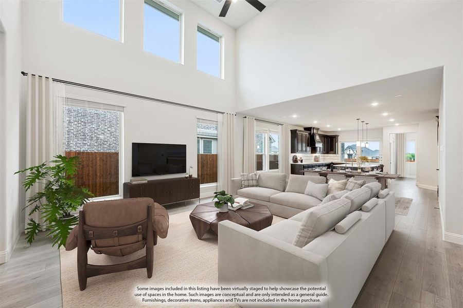 Open-concept living room with two-story ceilings, large windows, sectional sofa, and kitchen visible in background