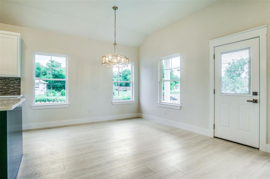 Unfurnished dining area with baseboards, vaulted ceiling, light wood finished floors, and a chandelier