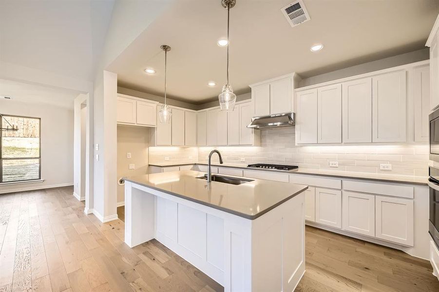 Kitchen with sink, white cabinets, hanging light fixtures, and stainless steel gas stovetop